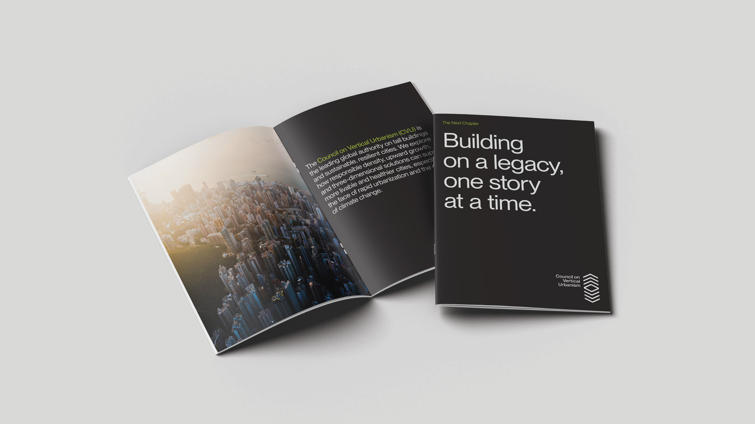 Open brochure on a light gray white surface displaying the Council on Vertical Urbanism brochure. Left page shows a cityscape with sunlight. Right page has text: "Building on a legacy, one story at a time" on a black background.
