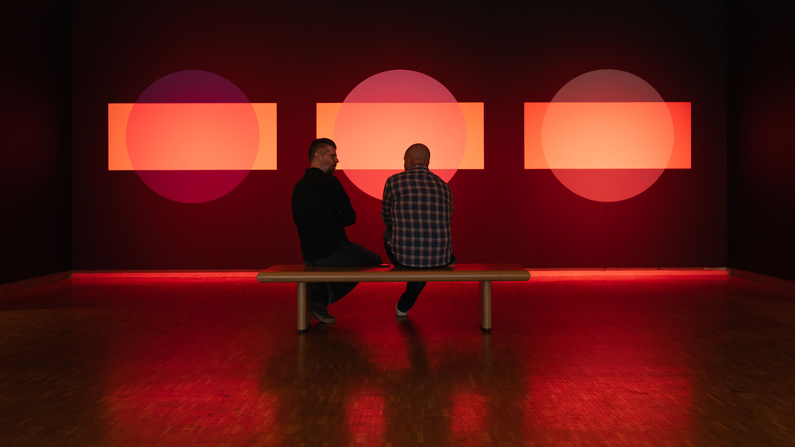 Two Multiple team members sitting on a bench in a museum having a converstion