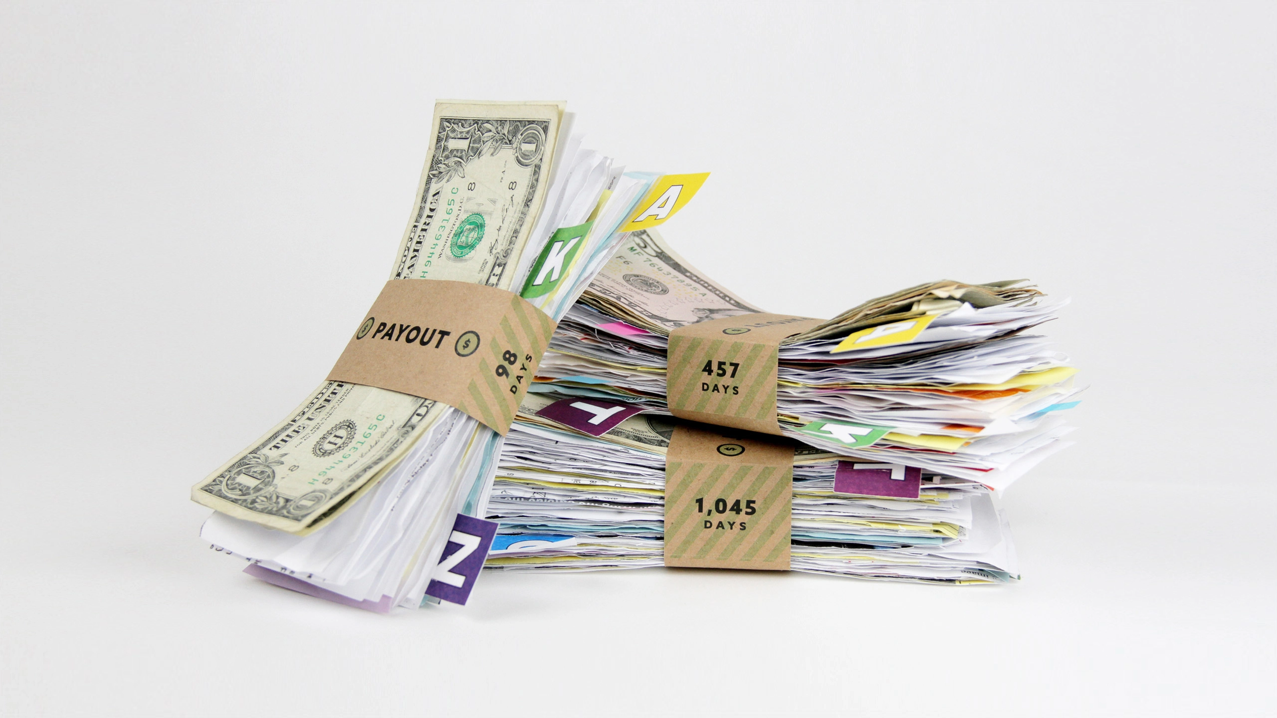 Stacks of neatly bundled paper and dollar bills with brown labels marked "Payout" and various numbers, symbolizing financial management and accumulation.